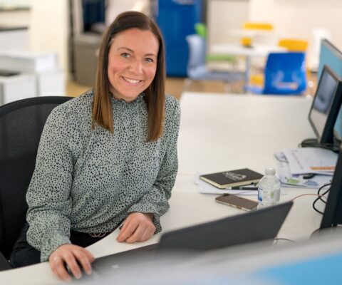 Woman at desk smiles for photograph.