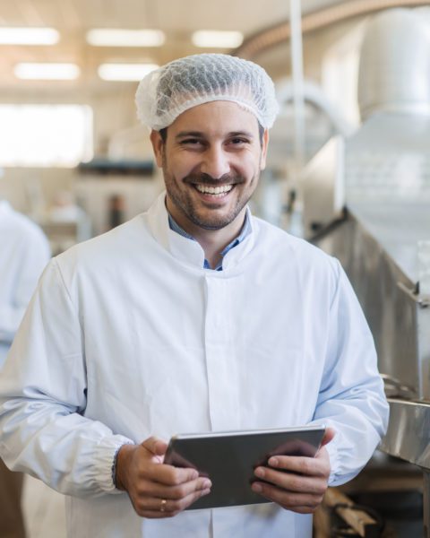 man smiling at the camera in a hair net holding a tablet