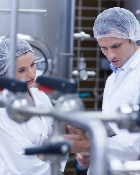 two people in hair nets holding a clipboard in a factory